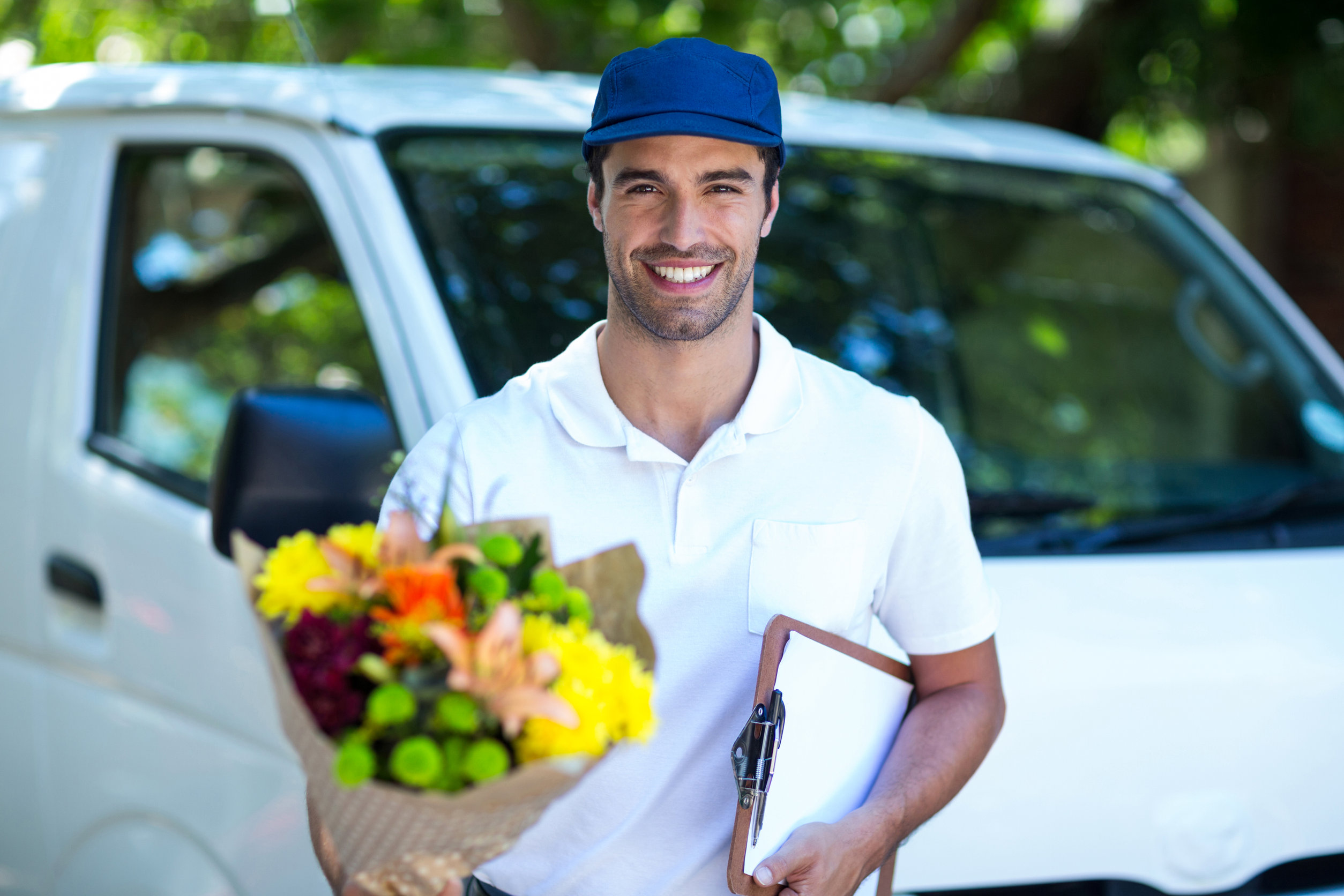 Portrait of smiling delivery man holding flower bouquet and clipboard while standing by van